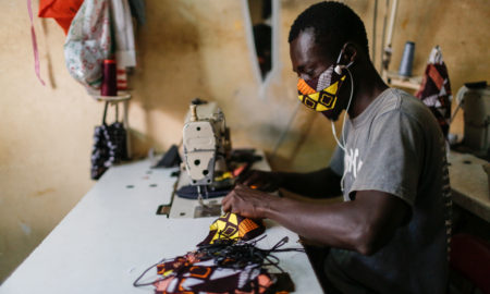 un tailleur porte un masque entrain de coudre