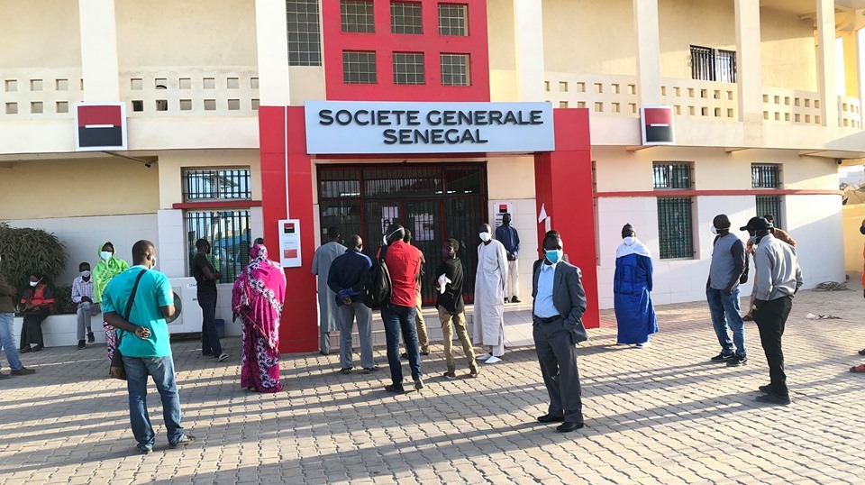 des clients portent des masquent patientent devant une banque à Dakar