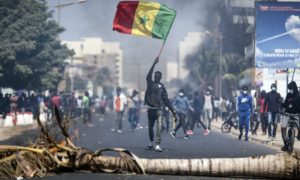 Un jeune manifeste en soulevant le drapeau du Sénégal