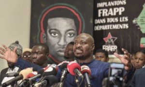 Un portrait d’Omar Blondin Diop est affiché derrière le militant sénégalais Guy Marius Sagna au siège du Front pour une révolution anti-impérialiste populaire et panafricaine (Frapp), à Dakar, le 25 mars 2021. SEYLLOU / AFP